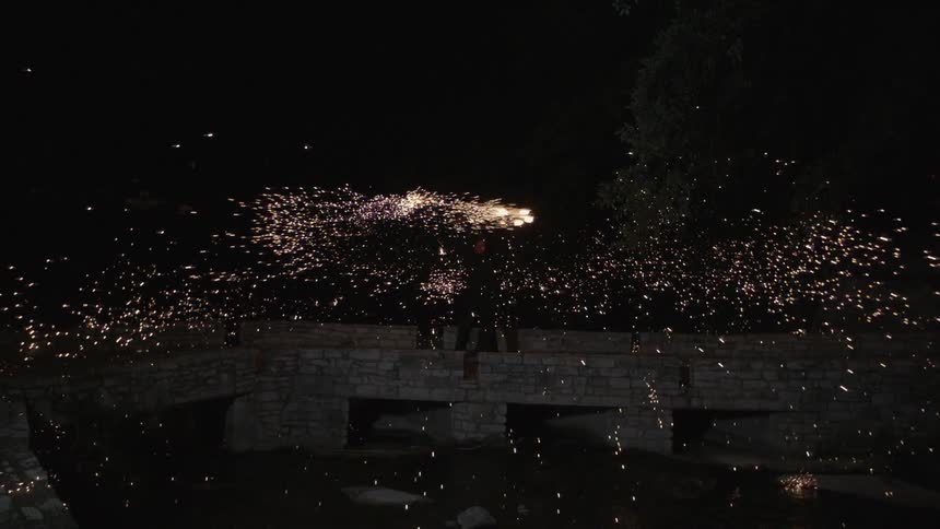 A person swinging a ball of flying sparks above their head,