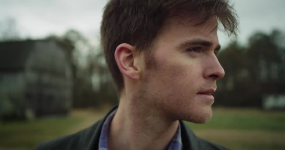 A man stands on a field looking around on a cloudy day
