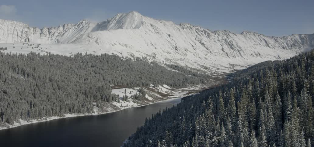 A river flows through snowy mountains covered in pine trees