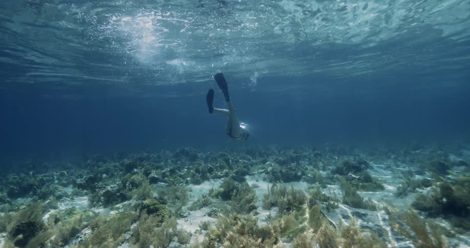 Female diver rotates underwater while her mask is reflecting the sun