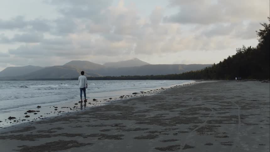 A man walks barefoot on the beach as waves come to shore