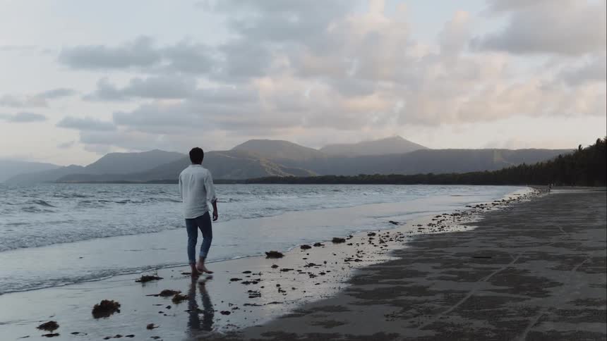 A man walks down the beach with the waves crashing over their feet