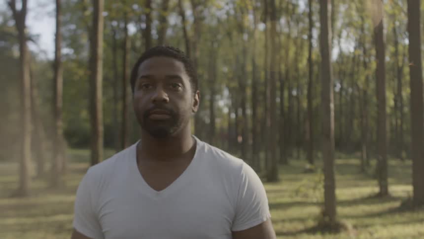Black man wearing white t shirt walks in the forest during daylight