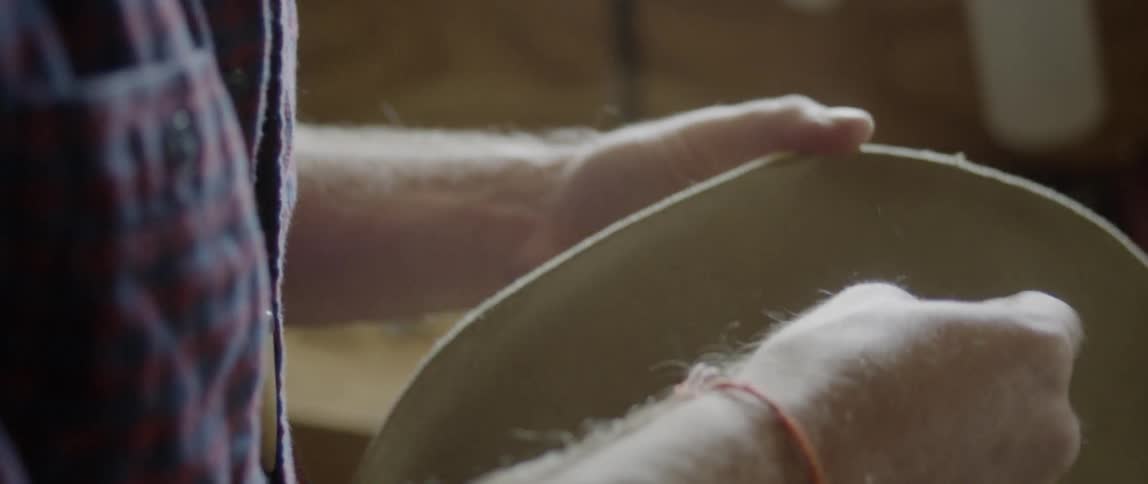Young adult man pushes a needle and thread through a cowboy hat