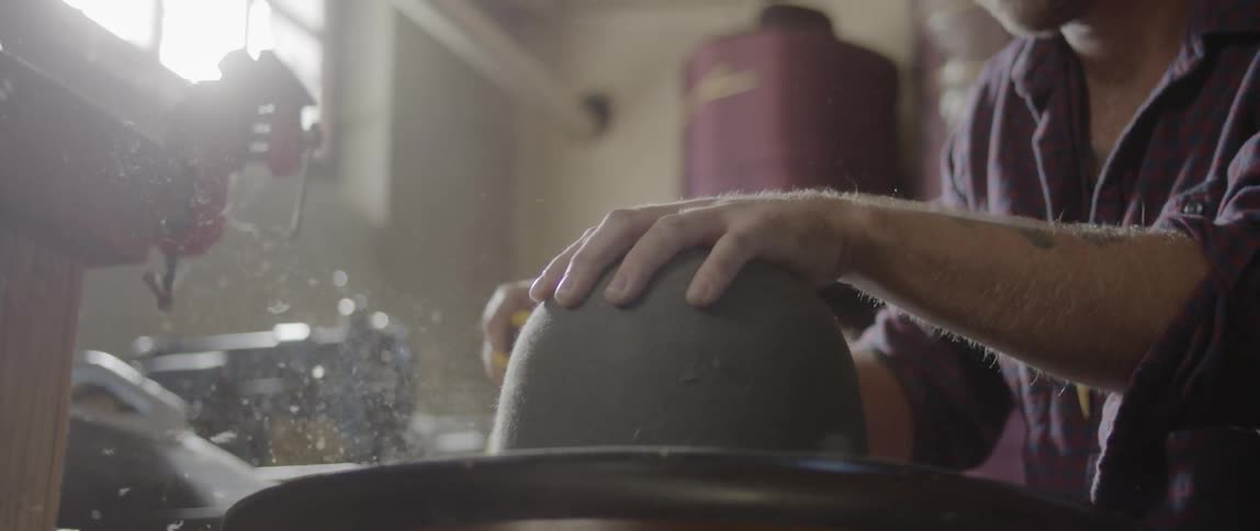 Man sanding a hat with a power tool on his workshop