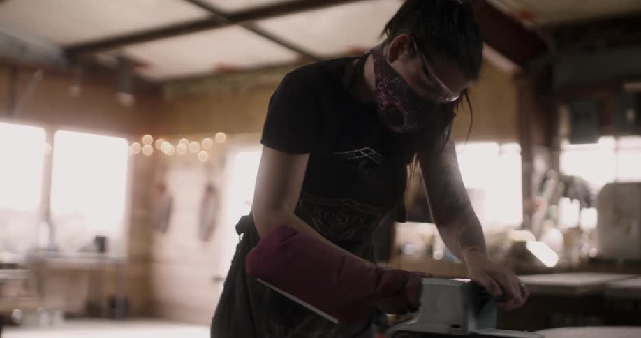 A woman in goggles and a mask using a power sander