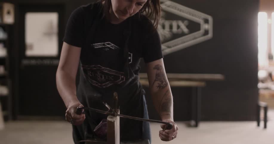 A woman uses a tool to shave off a section of a wood post