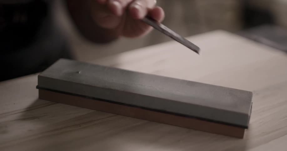 A woman sharpens a chisel along a sharpening block on a table