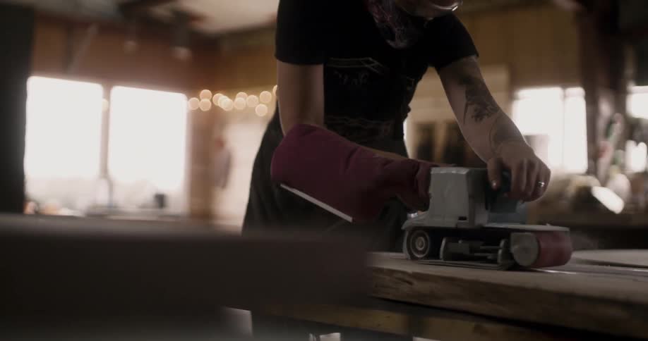 A female carpenter using a power sander on a wooden board