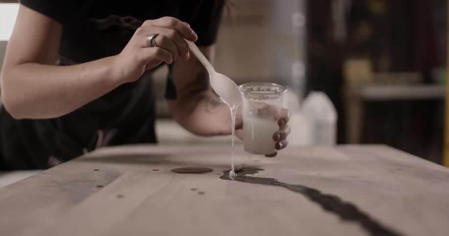 Woman pouring white liquid from a spoon into a crack on a slab of wood