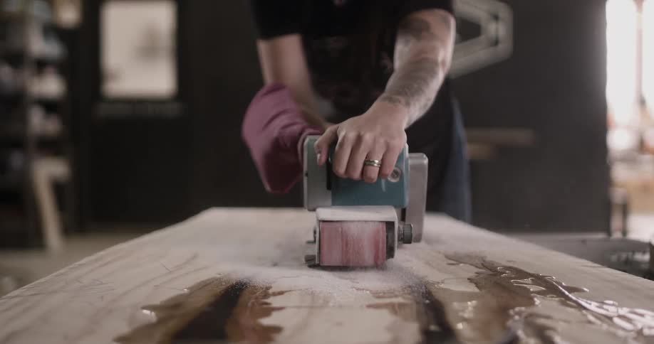 A man with tattoos on his arms moves a sander over a slab of wood