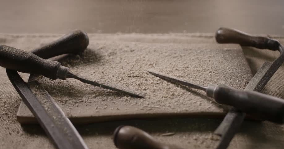 Wood shavings fall on top of a piece of wood and tools
