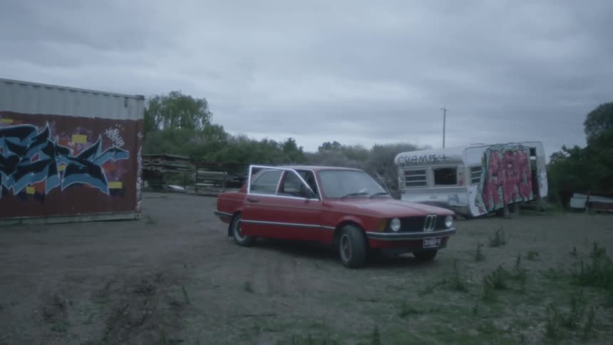 A cars passenger door hangs open behind a building with no people in sight