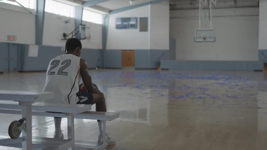 Football player sits on a bench on basketball court inside a empty thinkinggym