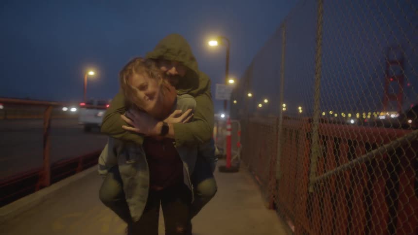 A girl carries a boy on her back walking on the sidewalk by a busy highway