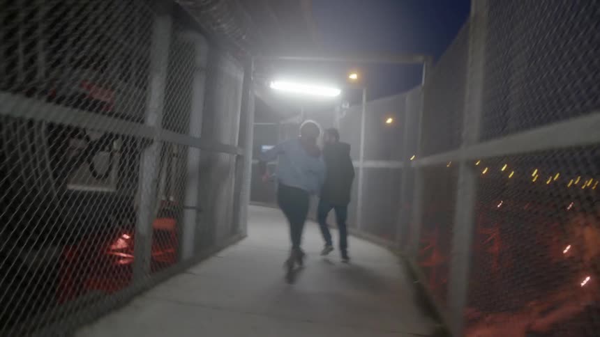 Two white people run down a fenced in corridor