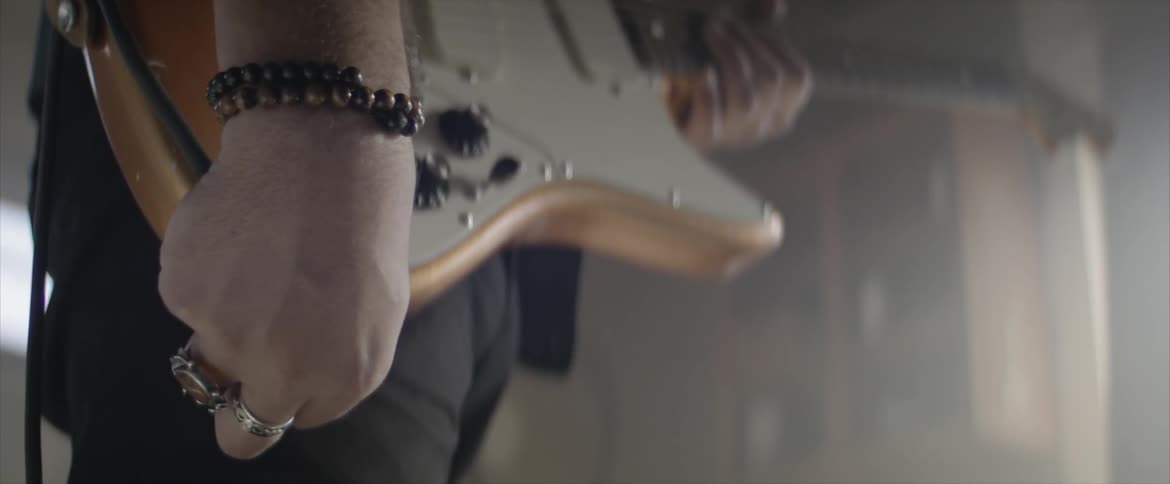 A man wearing two rings on his right hand plugs a guitar lead into his geronimo guitar