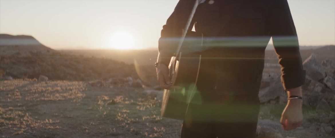 Man with guitar on a desert at sunset