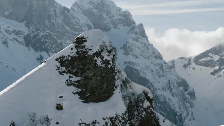 A cross stands on a snowy rocky peak