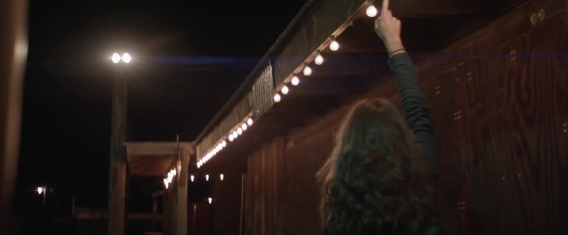 Woman touches hanging lights as she walks near building at night