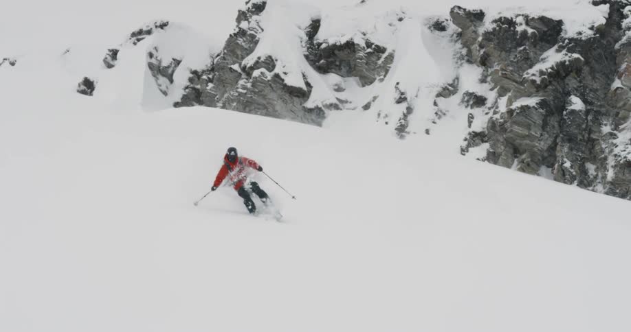 A skier in a red coat glides down a snowy mountainside