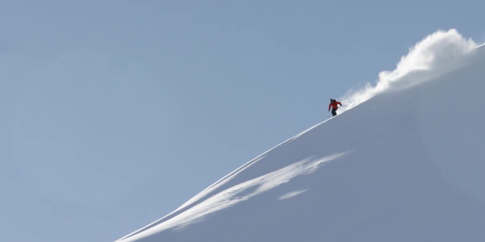 A skier flies down the side of a snow covered mountain