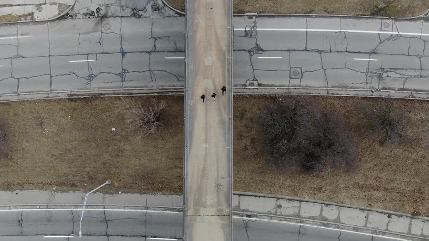 Three people are running on a pedestrian bridge over top a highway