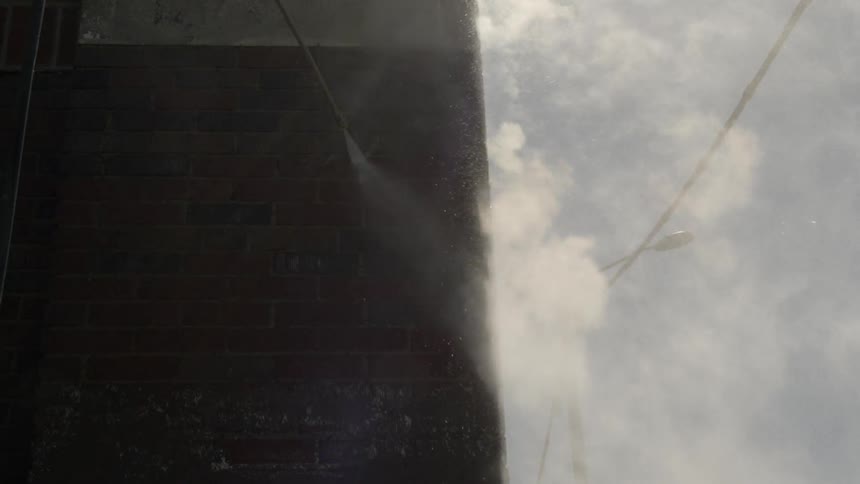 Someone uses power washer on a brick wall