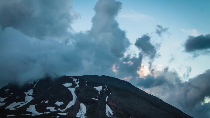 Clouds float over a snowy mountain ridge at sunset