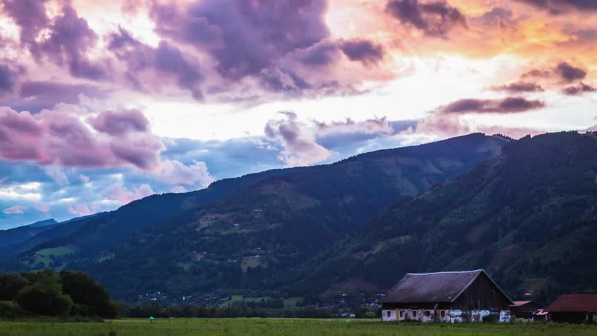 Clouds pass over hill tops and a farm house and field