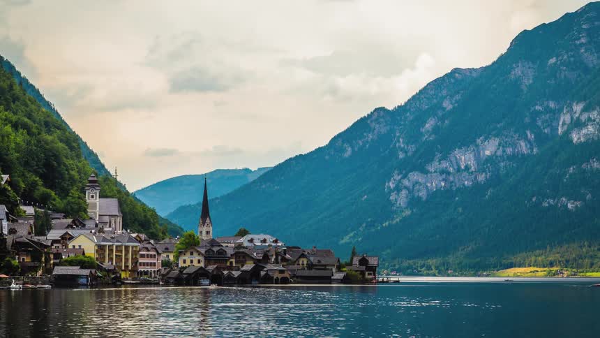 An austrian mountain town with a tall church spire sits on the edge of a lake