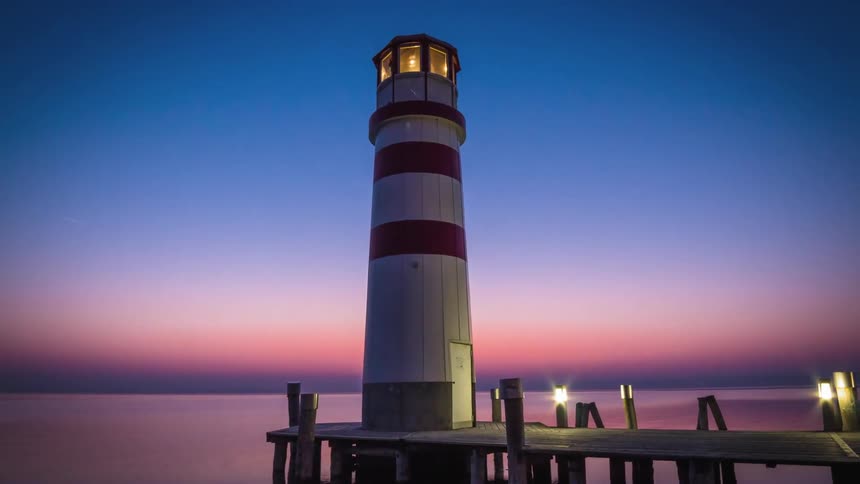 Lit lighthouse on lit pier at sunset