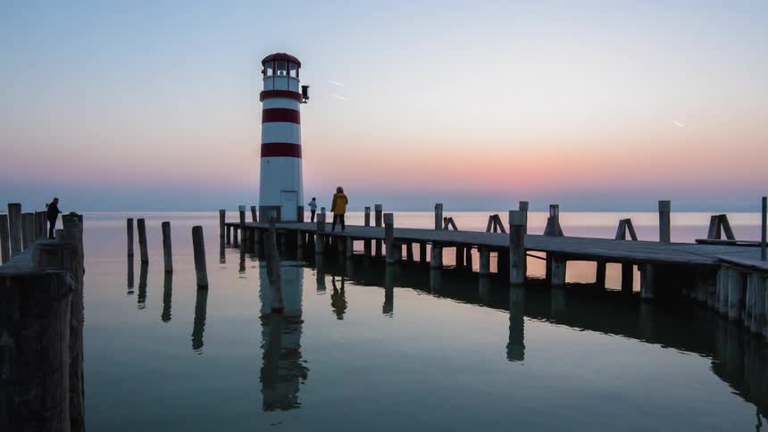 Views of the lighthouse where people walk around at the end of the pier at sunset