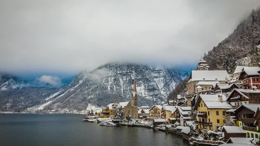 Boats leave and return from the dock of a small village at the base of snow dusted slopes