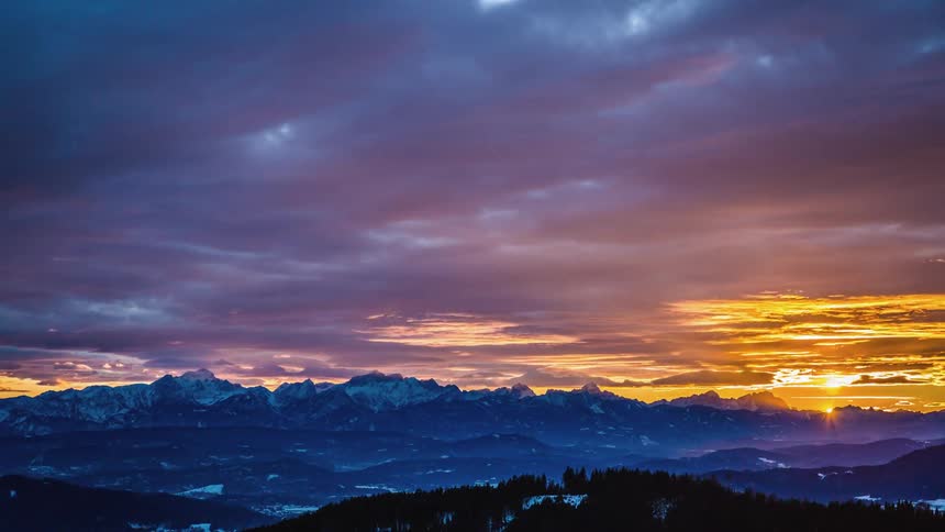 Sun sets over snow covered mountain range hills and forest