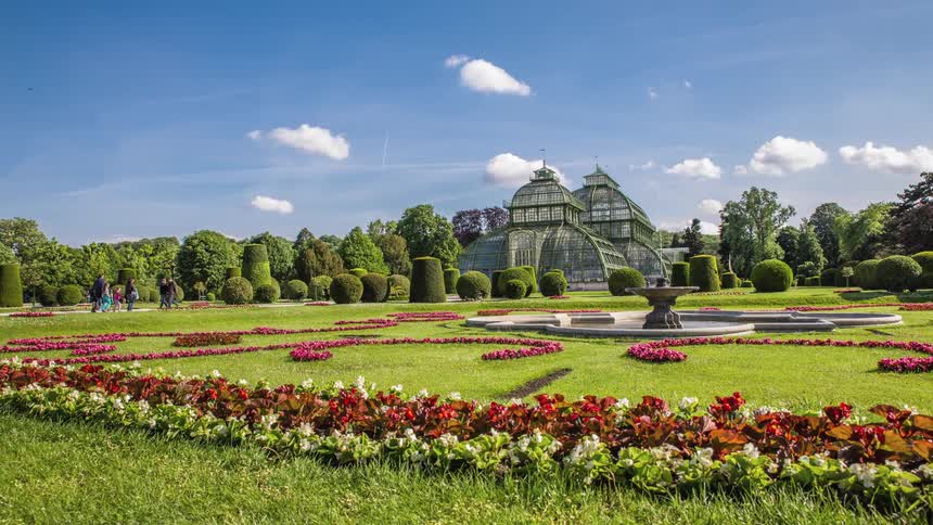 People walk on paths around beautifully manicured botanical gardens at the palm house in austria on a sunny day