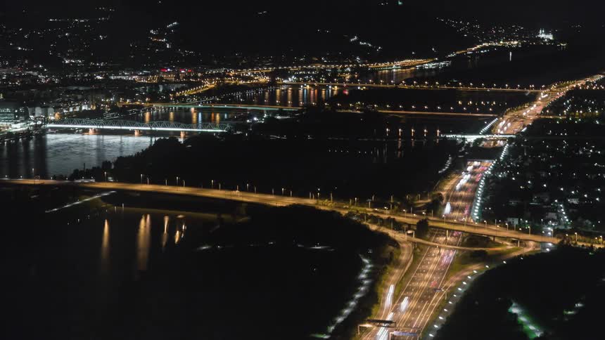 Cars drive across a bridge near a river in a city at night