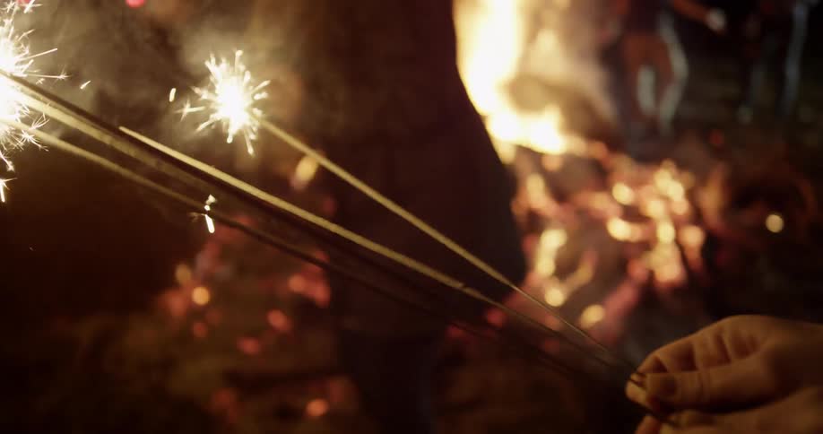 People are partying with sparklers around a campfire at night
