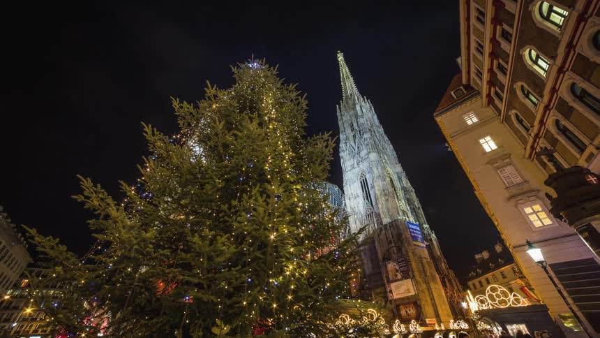 People walk around a tall christmas tree in a city at night