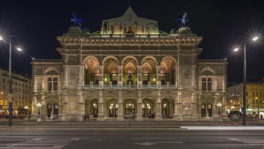 Vehicles pass by an ornate building in a city