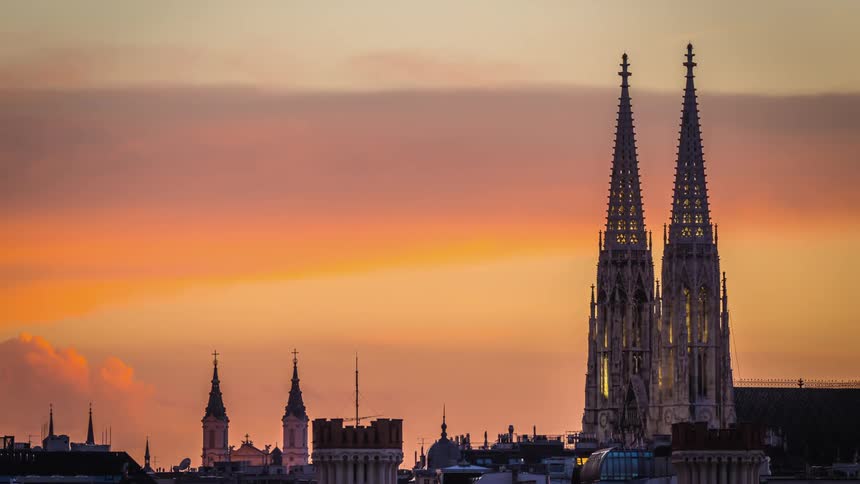 The clouds move behind large church steeples as the sun sets