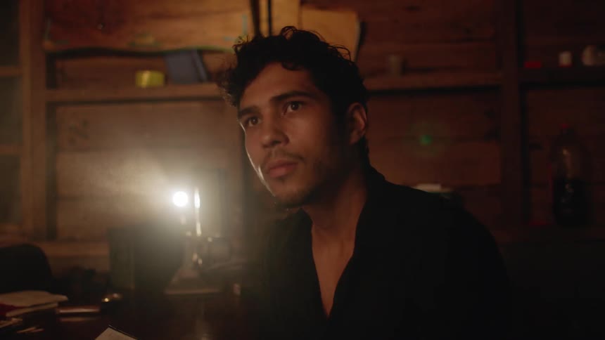 A man uses an old projector in a cabin while reading a book