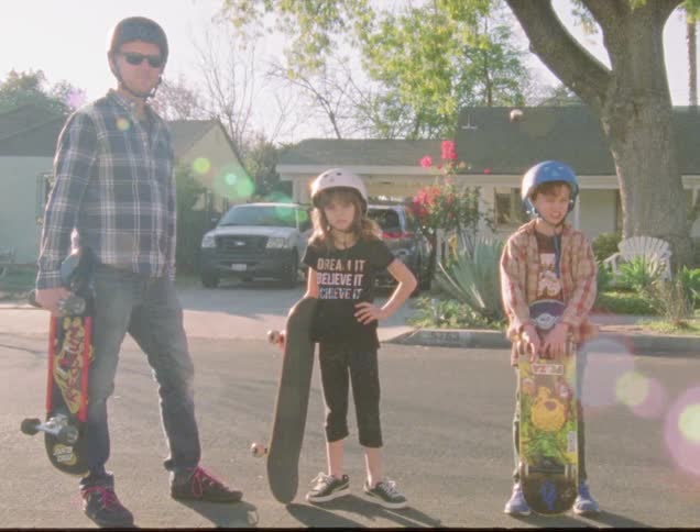 A man and two children stand on the street with skateboards and helmets