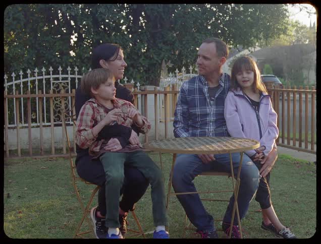 Man and woman sit at a table with their daughter and son in the garden late afternoon