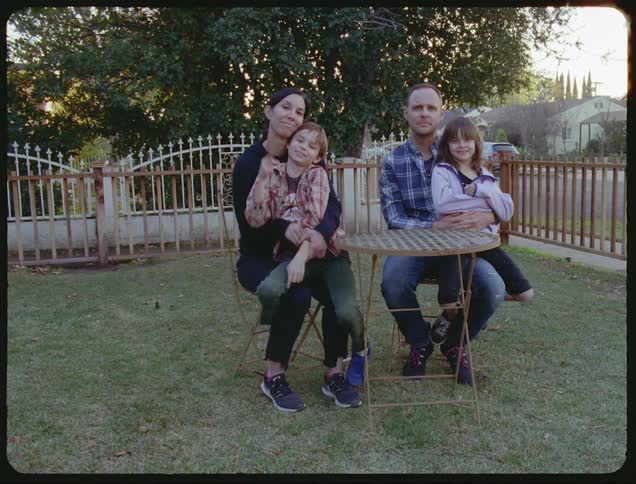 Man and woman sit at the table with their son and daughter in the garden during daylight