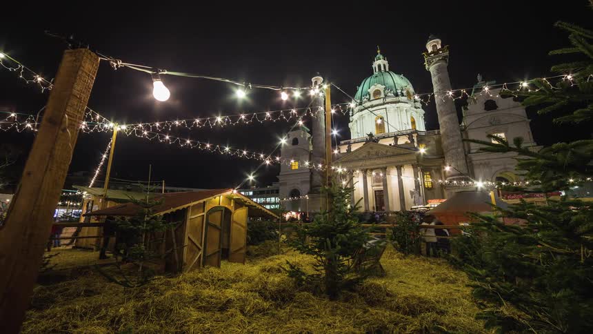 Busy garden by cathedral has people coming and going under the lit up garden under the night sky