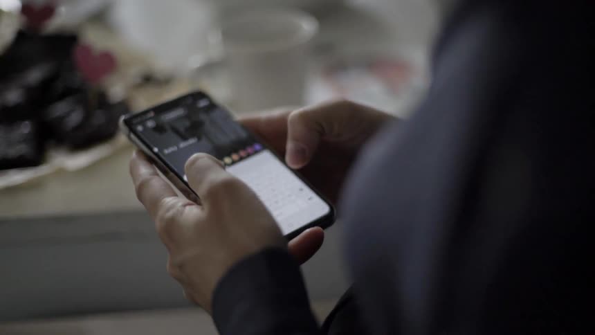 A man types on a smartphone while standing near a kitchen counter