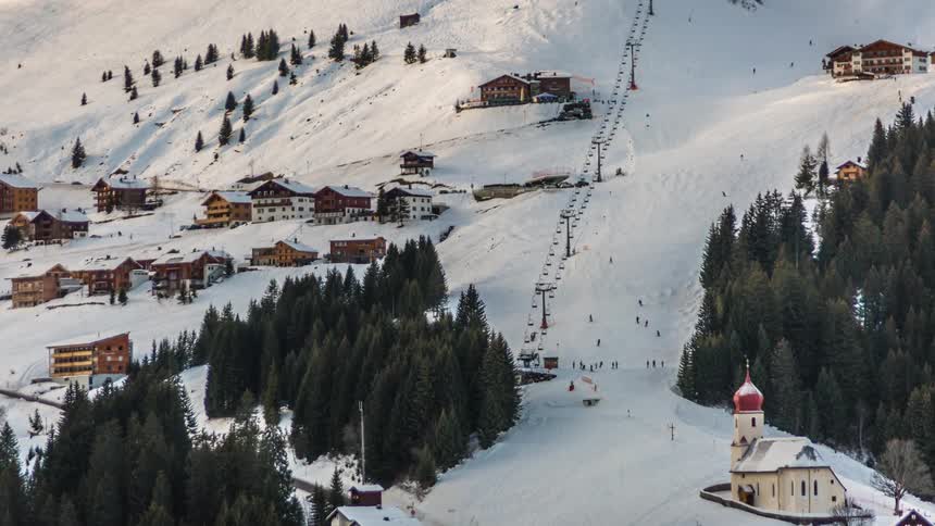 Hundreds of people ski down a mountain and travel along the resort area