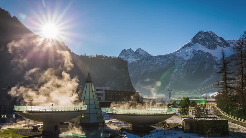 A facility with tanks of steaming liquid sits next to a road and in the shadow of mountains