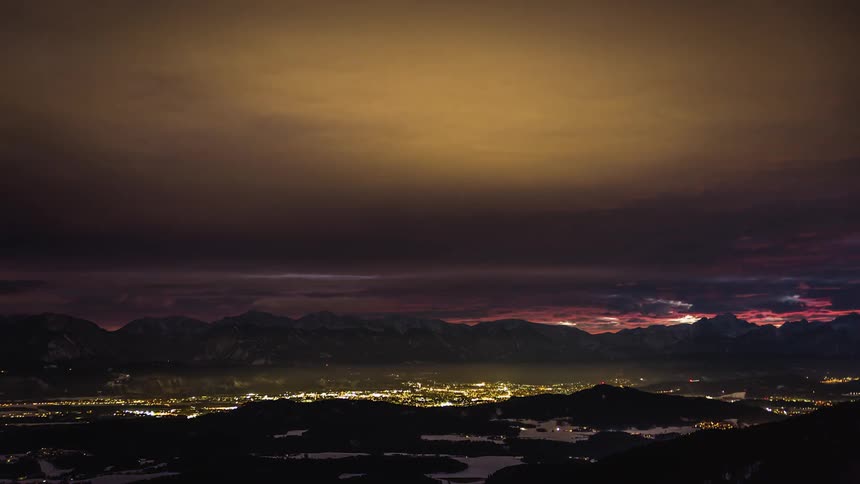 Red skies at night near the bright lights of a city surrounded by a mountain range